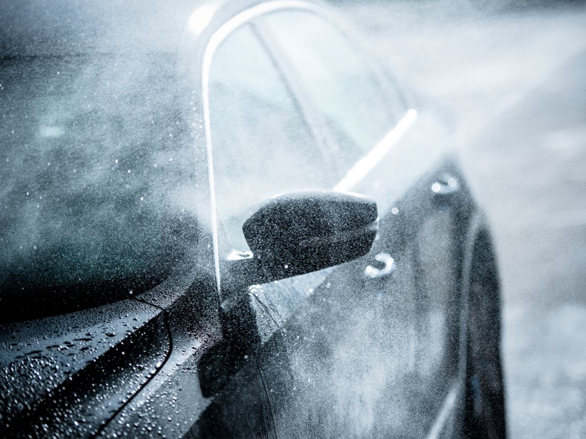 Außenspiegel eines dunklen Autos bei der Wäsche mit Sprühwasser