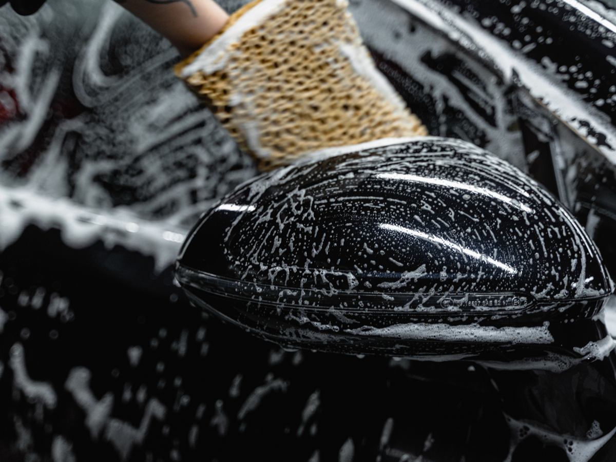 Außenspiegel eines schwarzen Autos wird mit Bürste und Schaum gewaschen