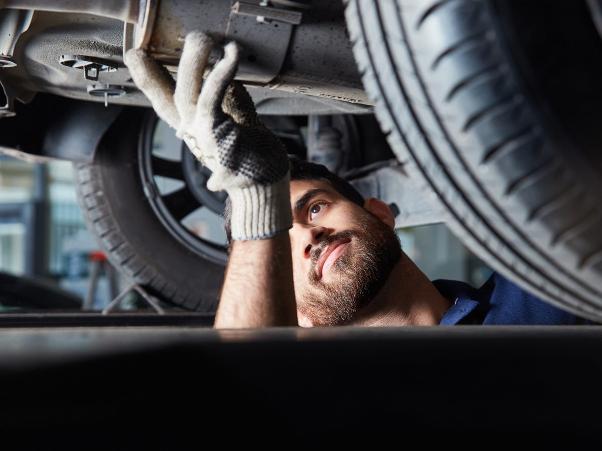 Mechaniker prüft die Abgasanlage unter einem Auto auf der Hebebühne