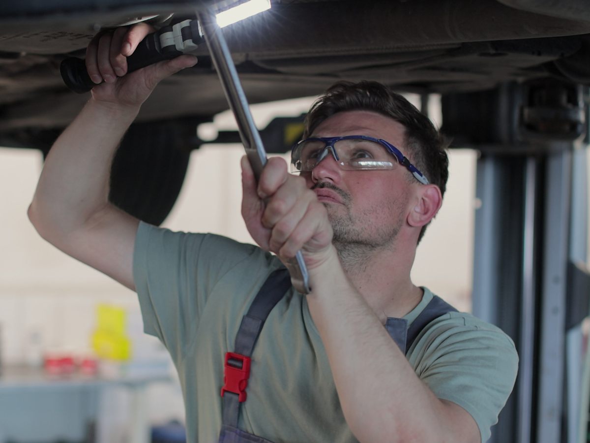 Mechaniker mit Schutzbrille arbeitet am Unterboden eines Autos