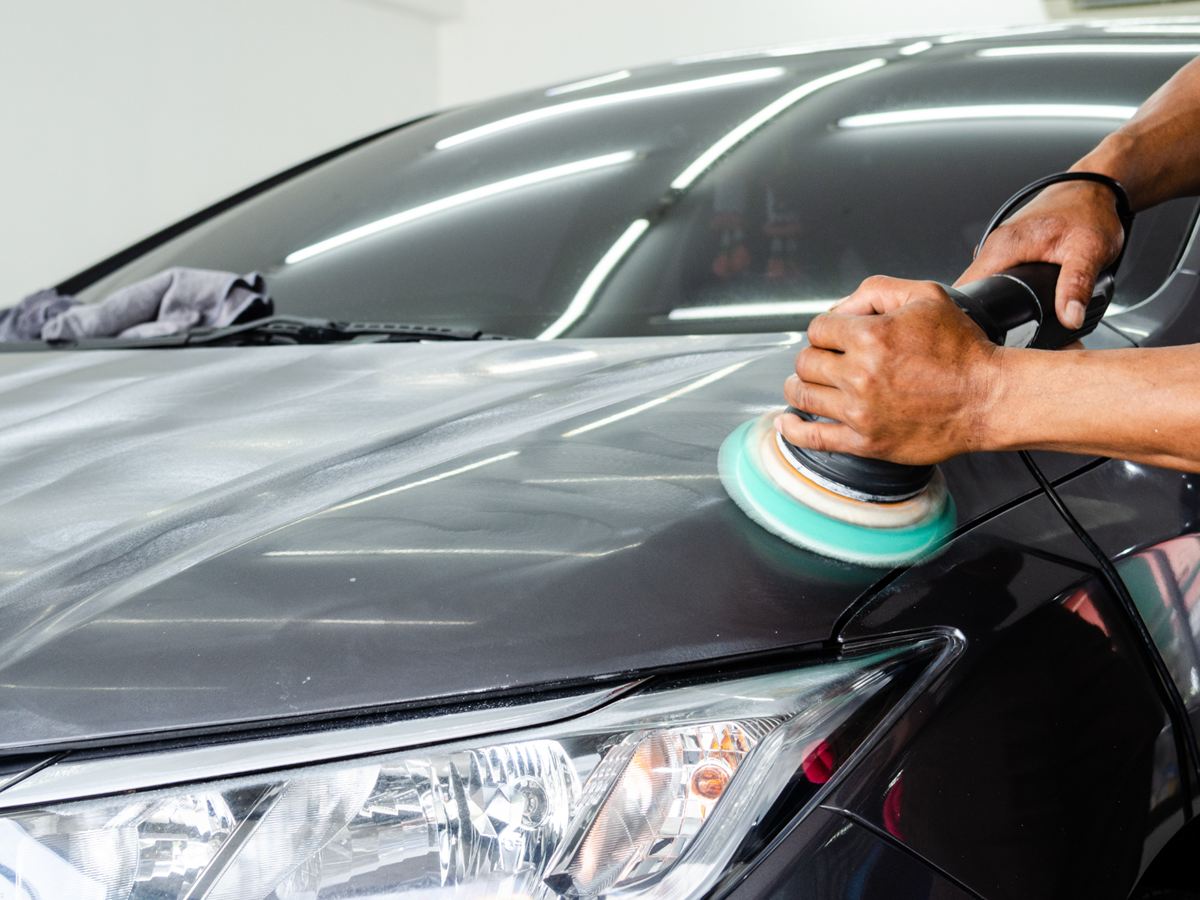 Motorhaube eines schwarzen Autos wird mit der Poliermaschine bearbeitet