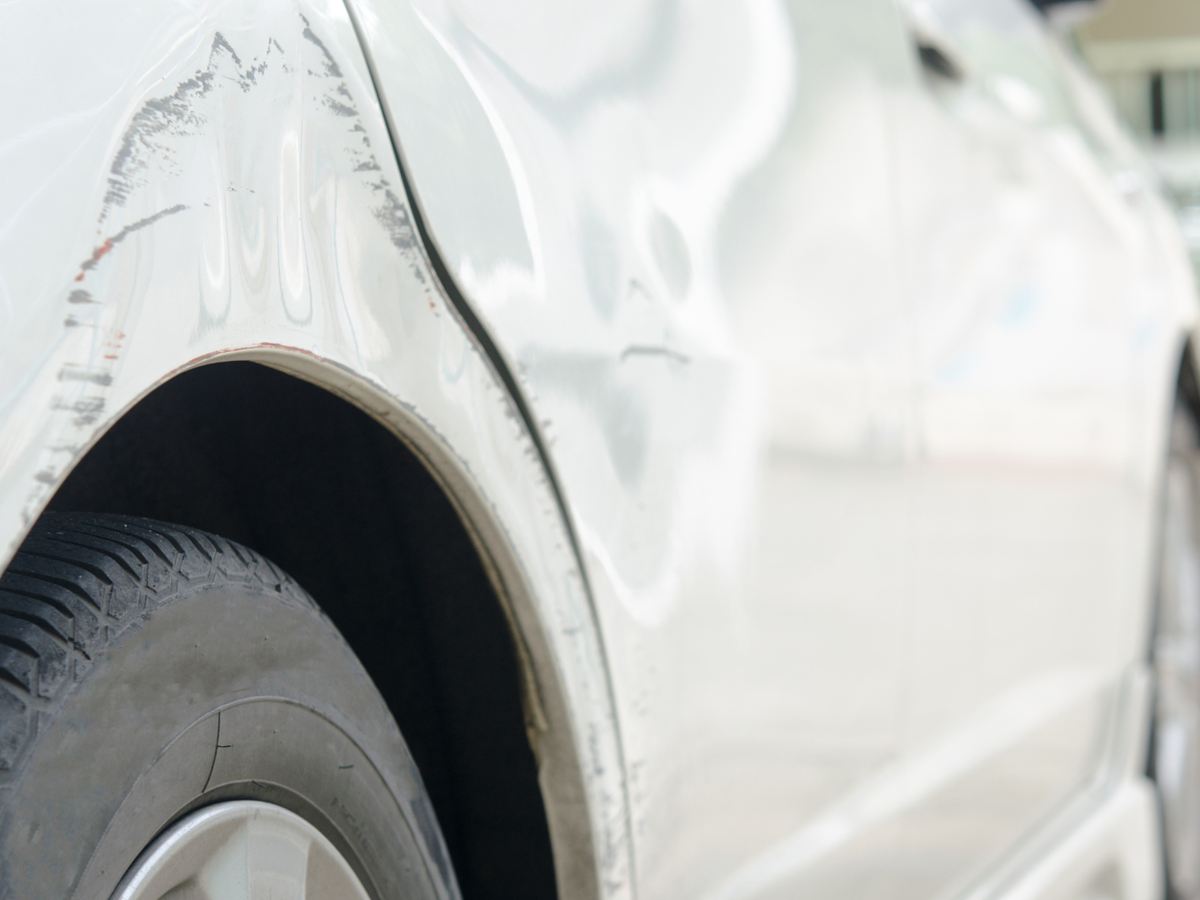 Delle und Kratzer am hinteren Radlauf eines weißen Autos