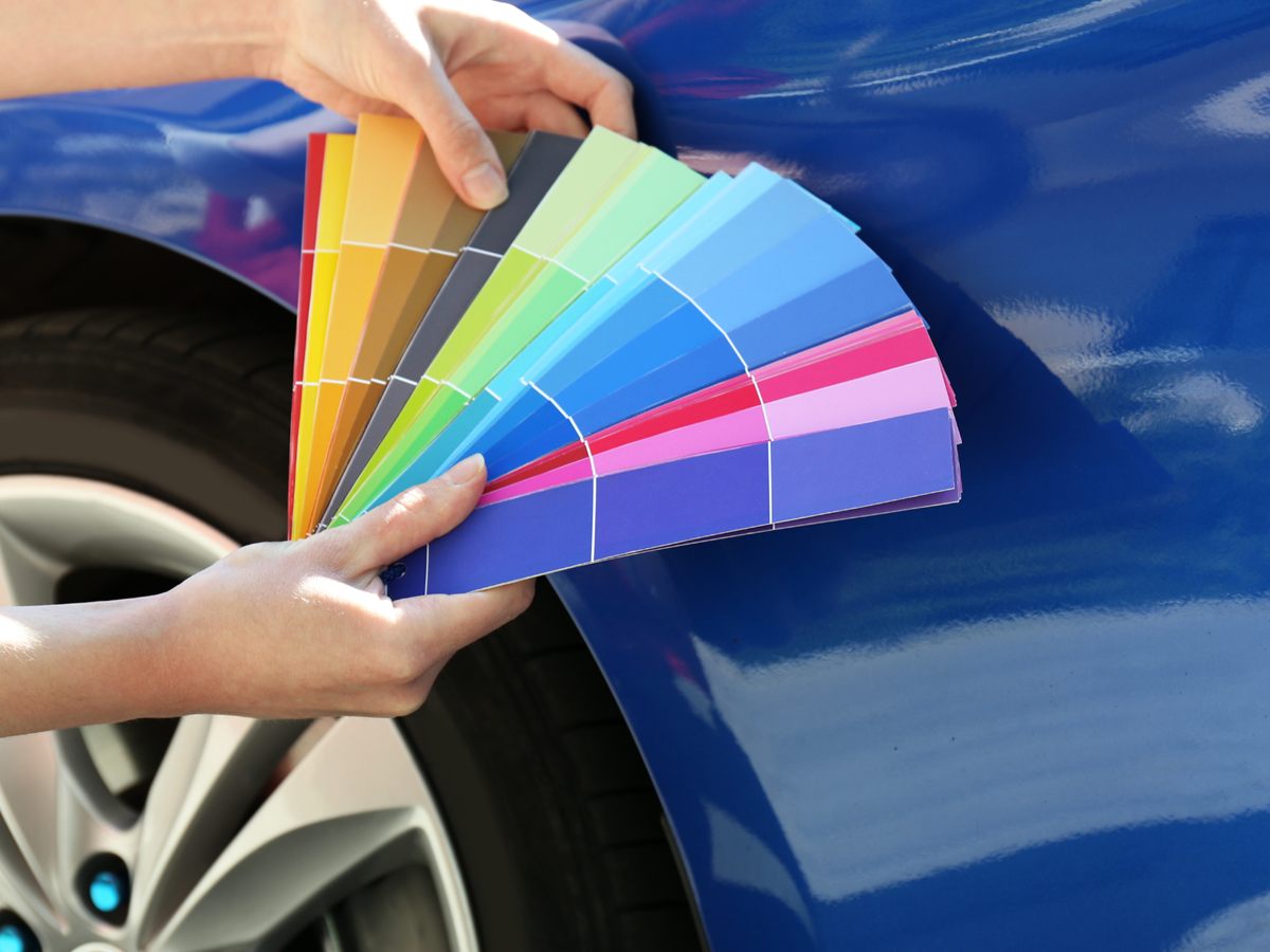 Farbfächer mit Lackmustern wird an ein blaues Auto gehalten