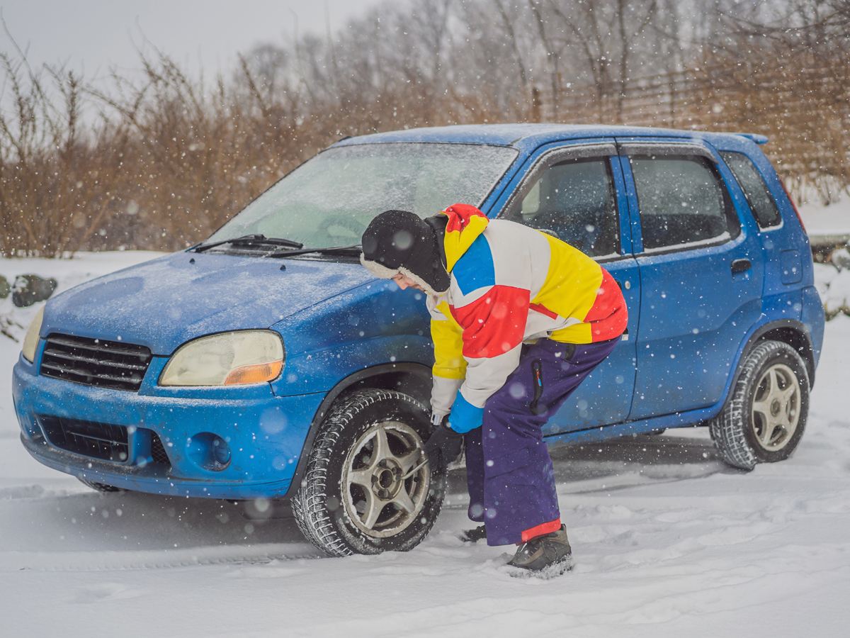 Person wechselt im Schneetreiben das Rad an einem blauen Auto